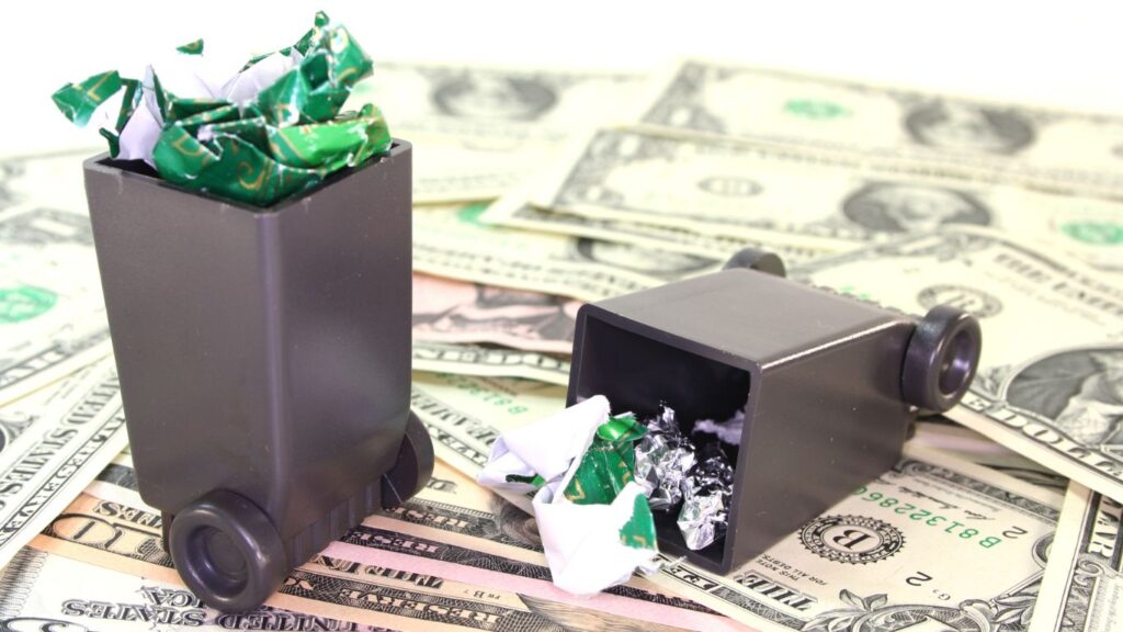 iniaturowe pojemniki na odpady na tle dolarów – symbol kosztów recyklingu i gospodarki odpadami w 2025 roku.