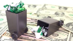 iniaturowe pojemniki na odpady na tle dolarów – symbol kosztów recyklingu i gospodarki odpadami w 2025 roku.